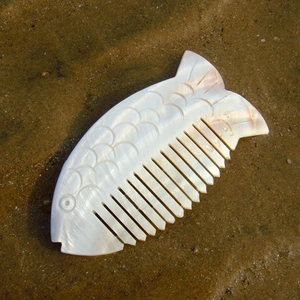 Handcrafted fish-shaped shell comb with pearlescent finish on a natural sandy beach