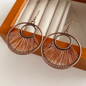 Detail of bohemian round hollow drop earrings with brown woven fan pattern on wood tray