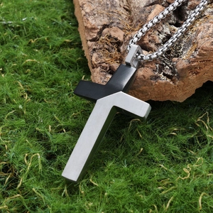 Detail of two-tone stainless steel cross pendant with brushed finish and box chain on moss