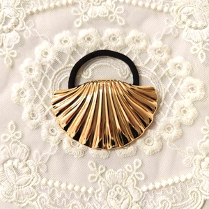Detailed view of a gold metallic shell hair tie resting on delicate white lace fabric