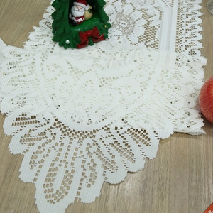 White lace Christmas table runner with delicate hollow embroidery on light wood surface