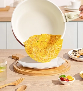Cream non-stick frying pan with detachable handle pouring a fried egg onto a white plate