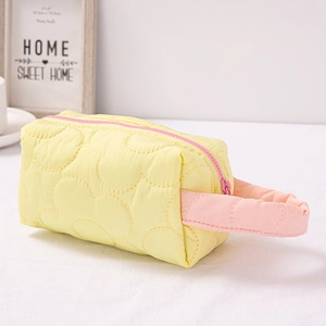 Quilted yellow makeup bag with pink zipper and handle on a minimalist white background