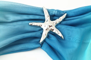 Dettaglio macro di un accessorio a stella marina argento con tessuto blu su fondo bianco