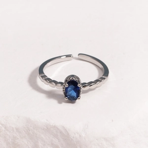 Detail of silver adjustable ring featuring a deep blue oval gemstone on white rock