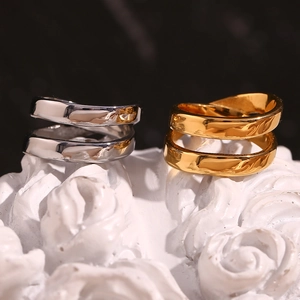 Minimalist double-layer cross rings in gold and silver finish on textured white surface