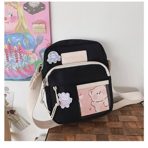 Détail du sac bandoulière en toile noire avec poches transparentes et badges mignons