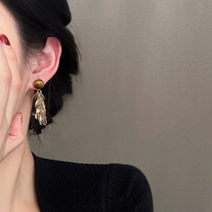 Detail of tiger eye leaf tassel earrings worn by a model against a textured wall