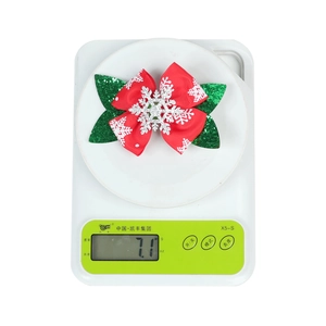 Detail shot showing 7.1g weight of glittery Christmas bow clip on a scale