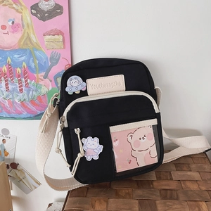 Détail du sac bandoulière noir en toile avec écussons de dessins animés et poche transparente