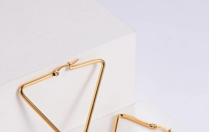 Detail of gold triangle hoop earrings showing slim tubular metal and secure pin closures