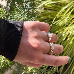 Detailed view of sterling silver pearl ring set worn against a lush green garden backdrop