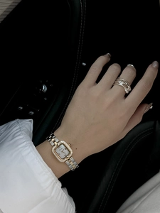 Détail d'une montre carrée en cristal et d'une bague creuse au poignet d'une femme