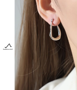 Close-up of a silver irregular streamlined stainless steel hoop earring on a model
