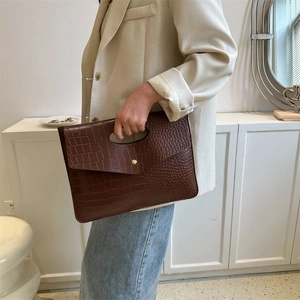 Brown crocodile embossed tote bag with gold magnetic clasp shown in a modern home setting