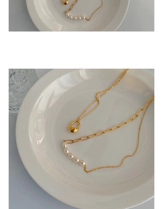 Detailed shot of a gold mixed-link chain necklace with five pearls on a white ceramic tray