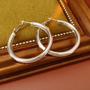 Polished silver hoop earrings displayed on a brown surface with a green velvet backdrop