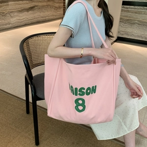Pink canvas tote bag with Maison 8 print worn by model on a rattan chair
