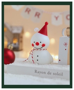 Détail d'une bougie bonhomme de neige avec chapeau rouge dans un décor d'hiver festif