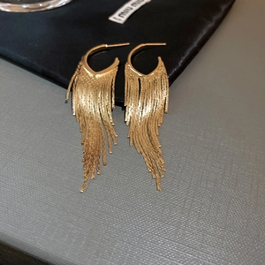 Close-up of elegant gold tassel earrings with shimmering chain fringes on a gray surface