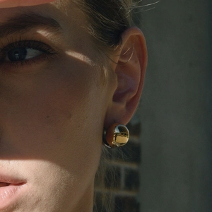 Close-up of a large gold hollow dome earring with a polished mirror finish on model