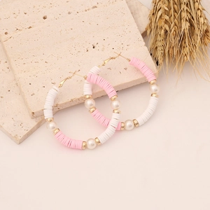 Detail of bohemian hoop earrings with pink heishi beads and pearls on stone surface