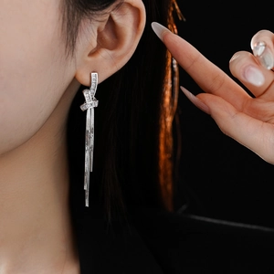 Close-up of silver knot tassel earrings with sparkling zircon stones on a female model