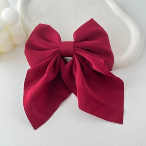 Detailed view of large burgundy satin bow hair clip with ribbons on a decorative tray