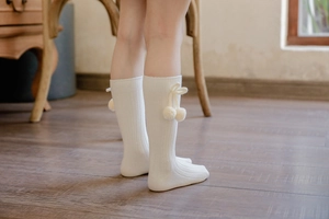 Detail of white knit knee-high baby socks with vertical stripes and plush ball bow