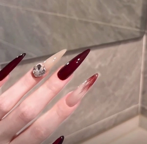 Macro detail of burgundy stiletto press-on nails with large crystals and marble patterns