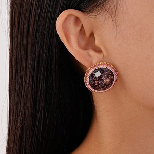 Gros plan d'une boucle d'oreille ronde vintage avec gemme rouge et texture tissée rose