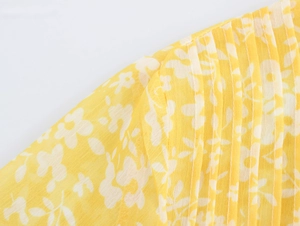 Detail of yellow floral dress fabric with delicate pleats and intricate white floral patterns