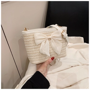 Close-up of cream woven bucket bag featuring large white chiffon bow and adjustable strap