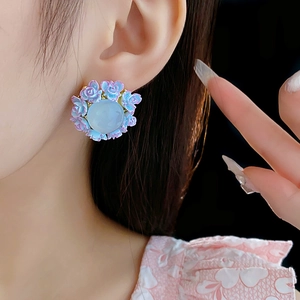 Close-up of floral stud earrings with blue cat-eye stone and pastel rose petals
