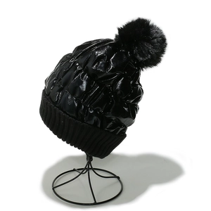 Detailed side view of black shiny down hat with faux fur pom pom and knit trim