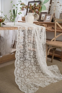 Detail of off-white lace table runner with floral embroidery hanging on vintage table