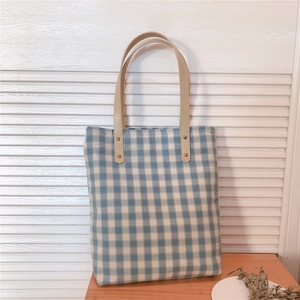 Detail of blue plaid canvas tote bag with brown leather handles and metal rivets