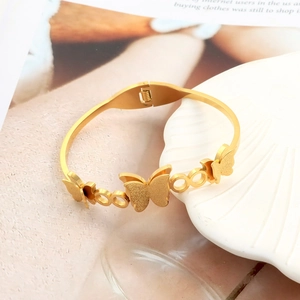Detail of gold butterfly bracelet with matte and polished finish on white shell tray