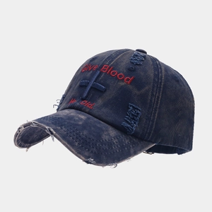 Detail of distressed navy blue denim baseball cap with cross embroidery and frayed edges
