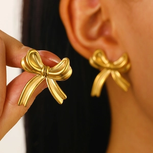 Detailed close-up of golden bow-shaped stainless steel stud earrings on an ear
