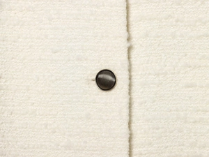 Macro-opname van bronzen metalen knoop met concentrische textuur op beige tweed stoffen jas