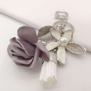 Macro detail of purple fabric rose, white tassel, and rhinestone enamel flower keychain