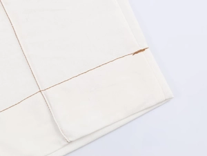 Detail of contrast stitching on white high-waisted flared trousers hem with brown thread