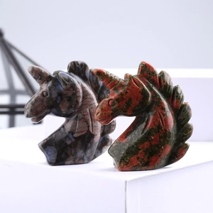 Macro shot of hand-carved natural crystal and gemstone unicorn heads on white pedestals