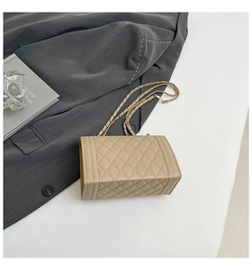 Detail of beige quilted flap bag with metallic chain strap and lock on a grey suit