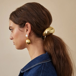 Close-up of golden metal ponytail cuff and pearl drop earrings on a female model