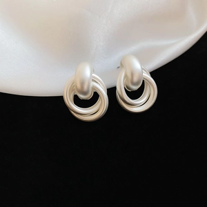 Detailed view of silver matte interlocking circular earrings on silk background