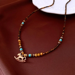 Détail du collier en œil de tigre avec pendentif cheval à bascule doré sur de la soie
