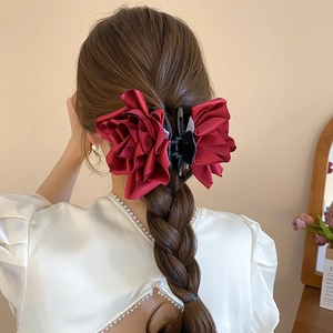 Détail d'une pince à cheveux rose en satin rouge foncé sur une coiffure tressée