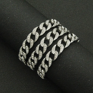 Detail view of silver Cuban link bracelets with clear rhinestones on a black stand